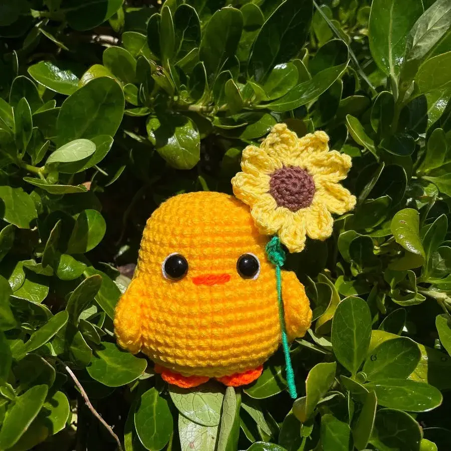 Pollito amigurumi amarillo sosteniendo un girasol tejido