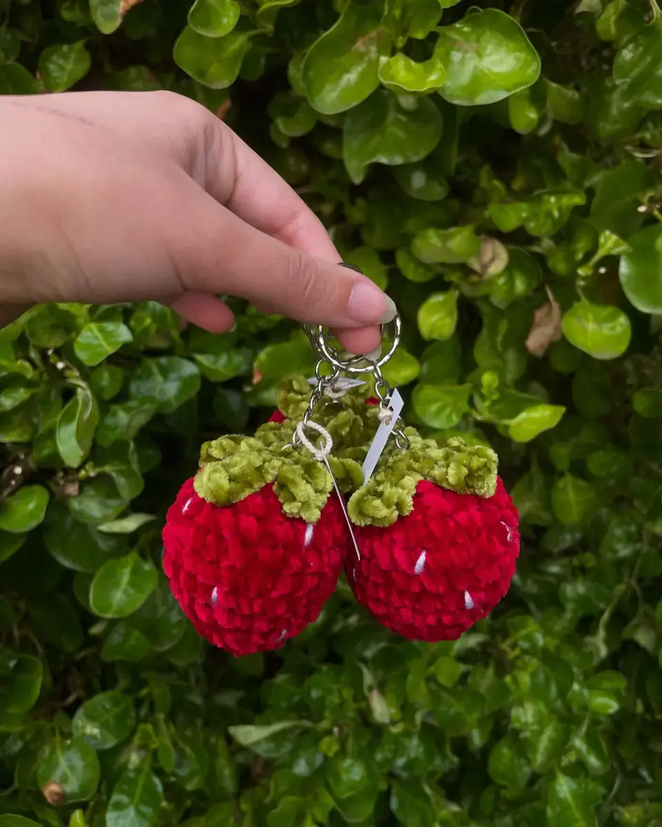 Dos frutillas tejidas de chenille colgando como llaveros
