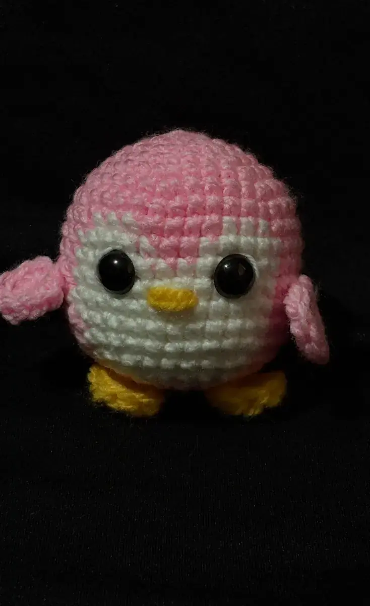 Pingüino rosado y blanco tejido sobre fondo negro